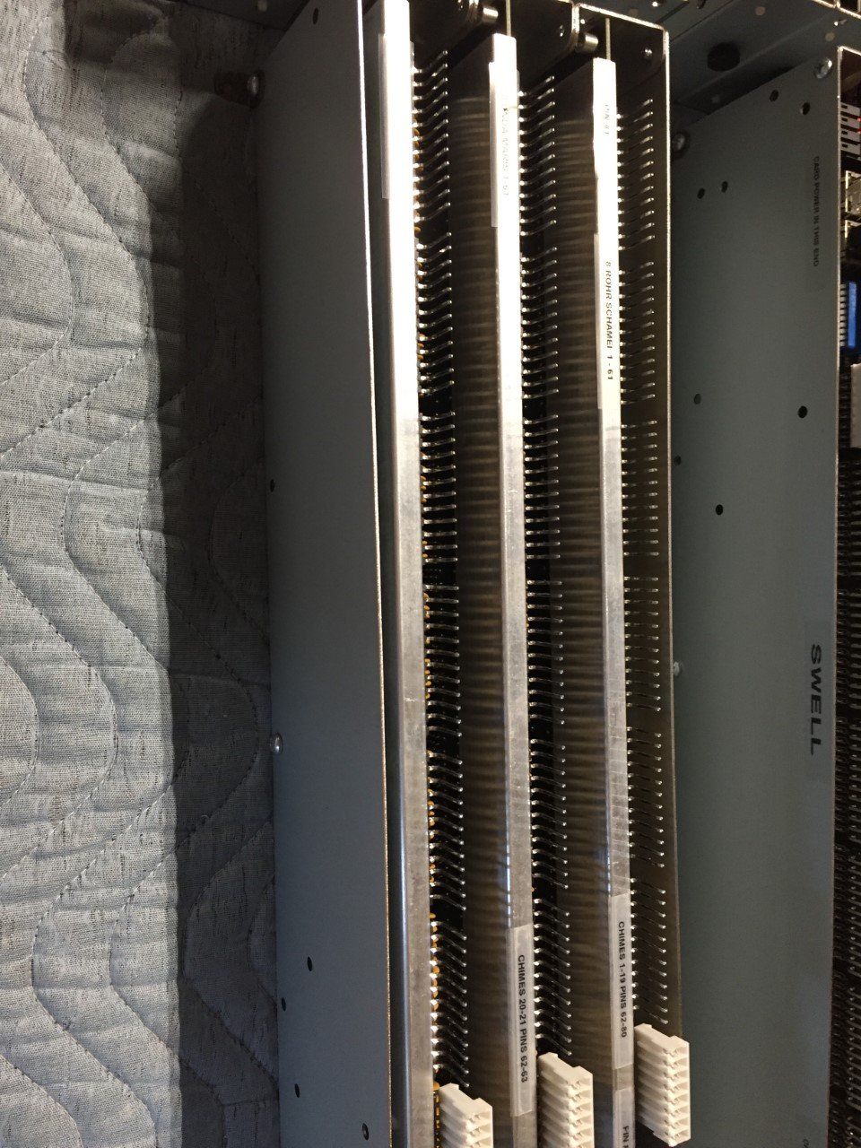 Close-up of a tall metal electrical component with copper contacts and a quilted gray pad behind it