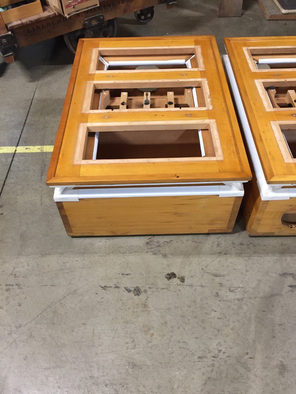 Wooden display case frames on a warehouse floor, with one box open and parts inside.