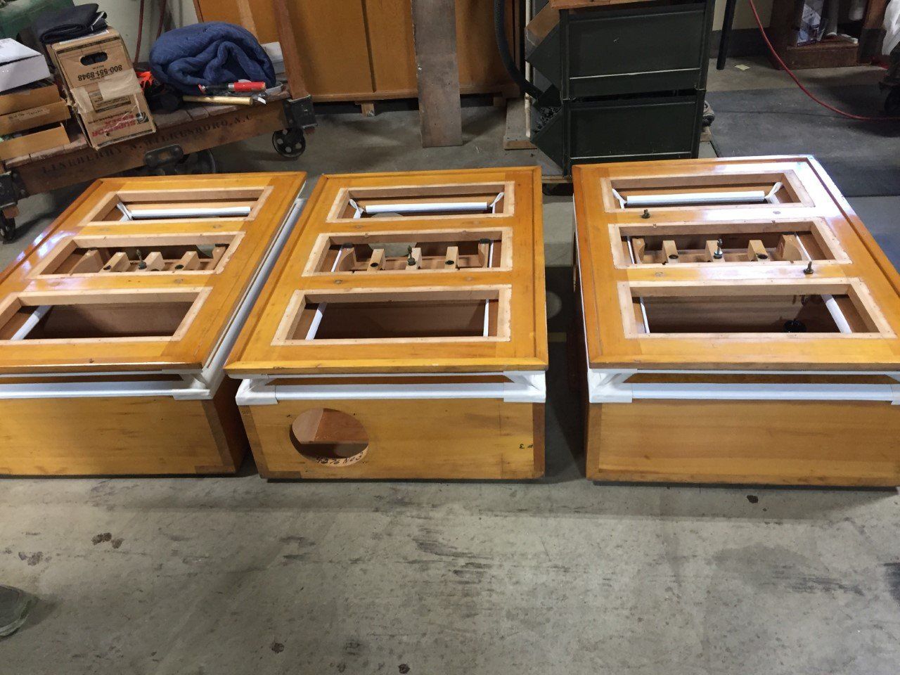 Three wooden hive boxes with framed sections, arranged on a garage floor.