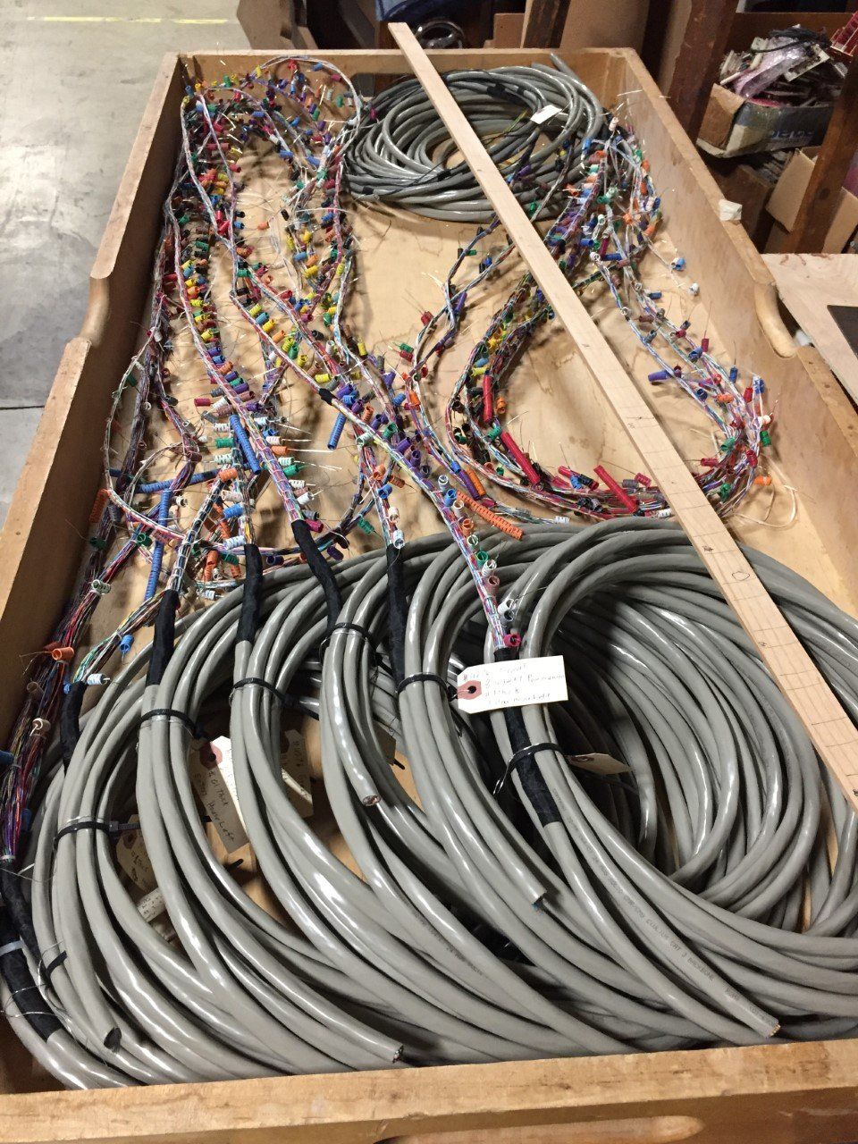 Coiled gray cables and colorful wires packed in a wooden crate, with wooden braces across the top.