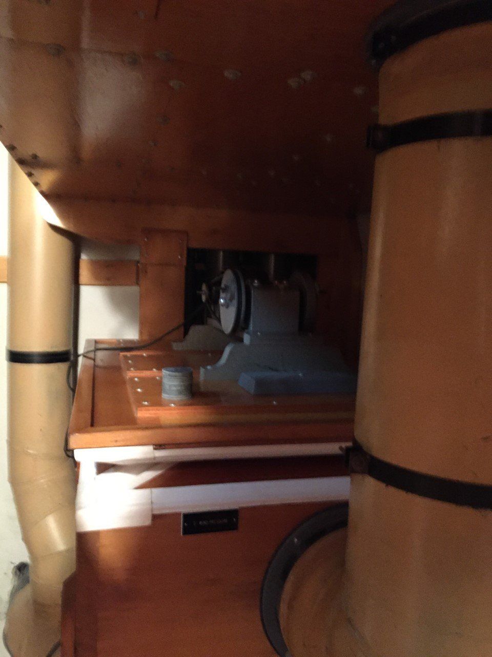 Narrow wooden interior with a small fan and shelves, viewed through a doorway or hatch