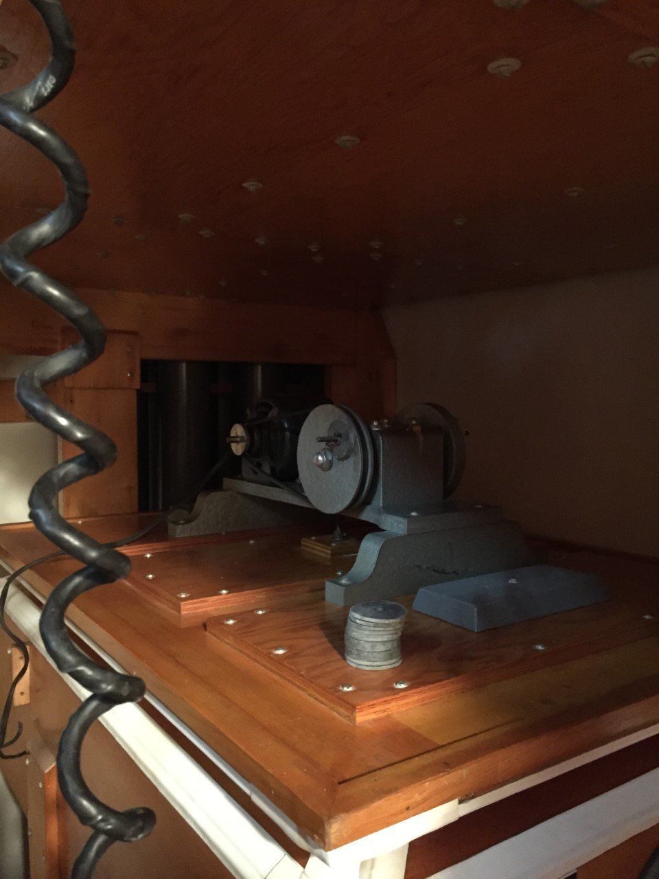 Coiled cable inside wooden cabinet, with a small fan and a cup on a shelf.