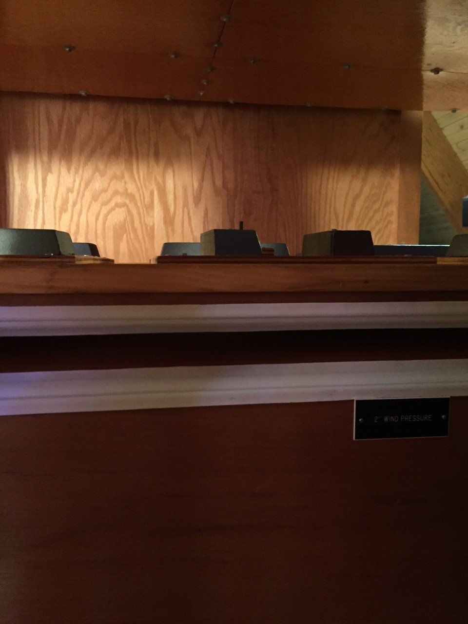 Wood-paneled shelf with three small dark objects and a lamp in the background