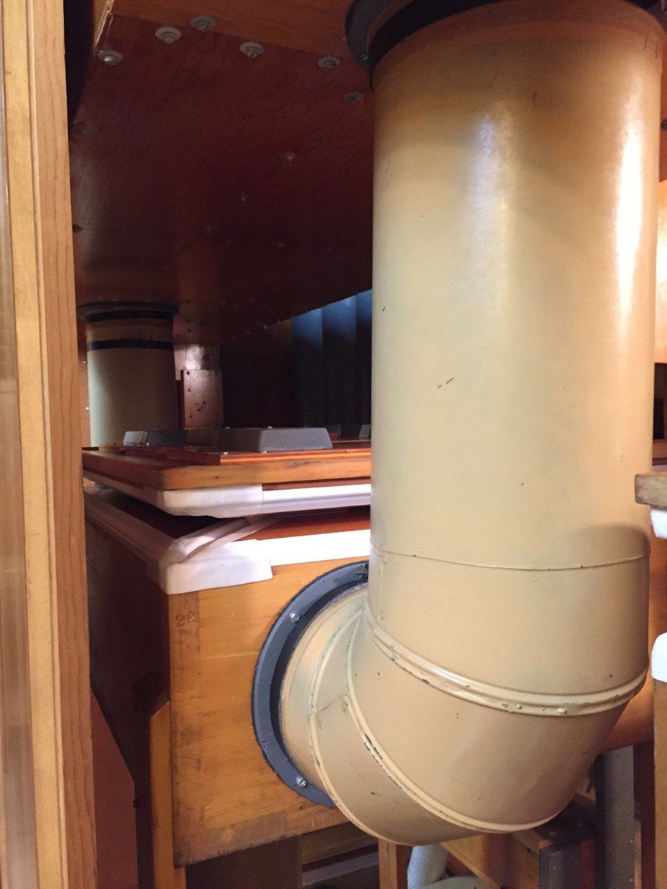 Close-up of beige plumbing pipe inside a wooden cabinet under a sink
