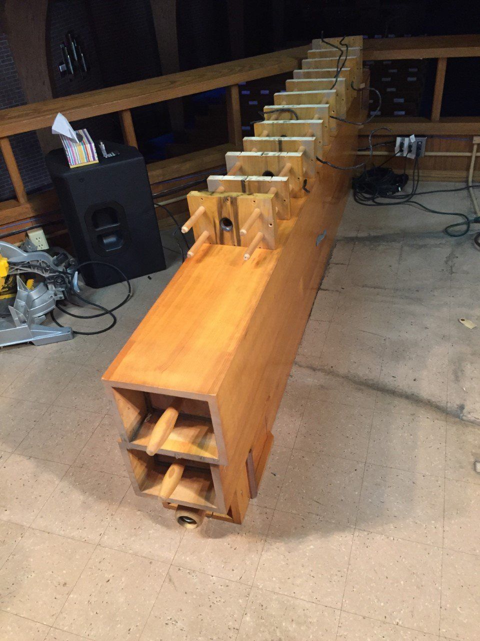 Long wooden beam with evenly spaced crosspieces on a concrete floor in a workshop-like space