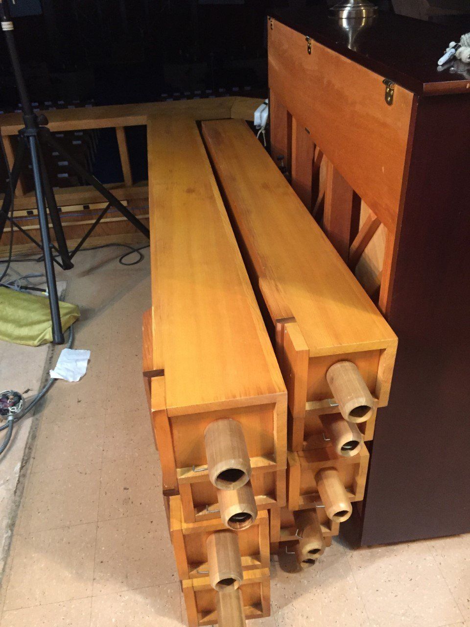 Stacked wooden organ pipes beside a piano in a dim room.
