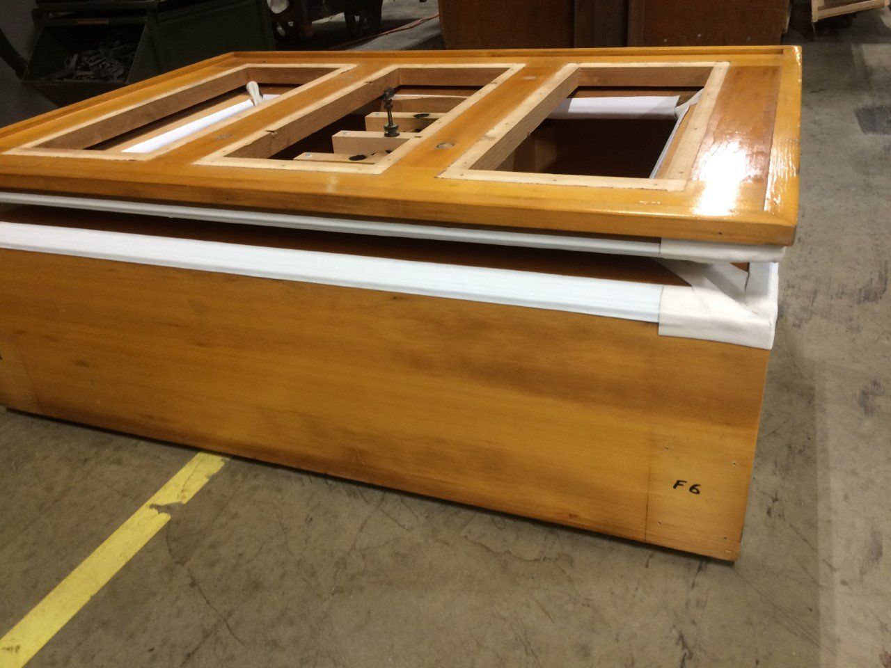 Wooden boat hull mold or display frame in a workshop, with polished wood panels on a concrete floor