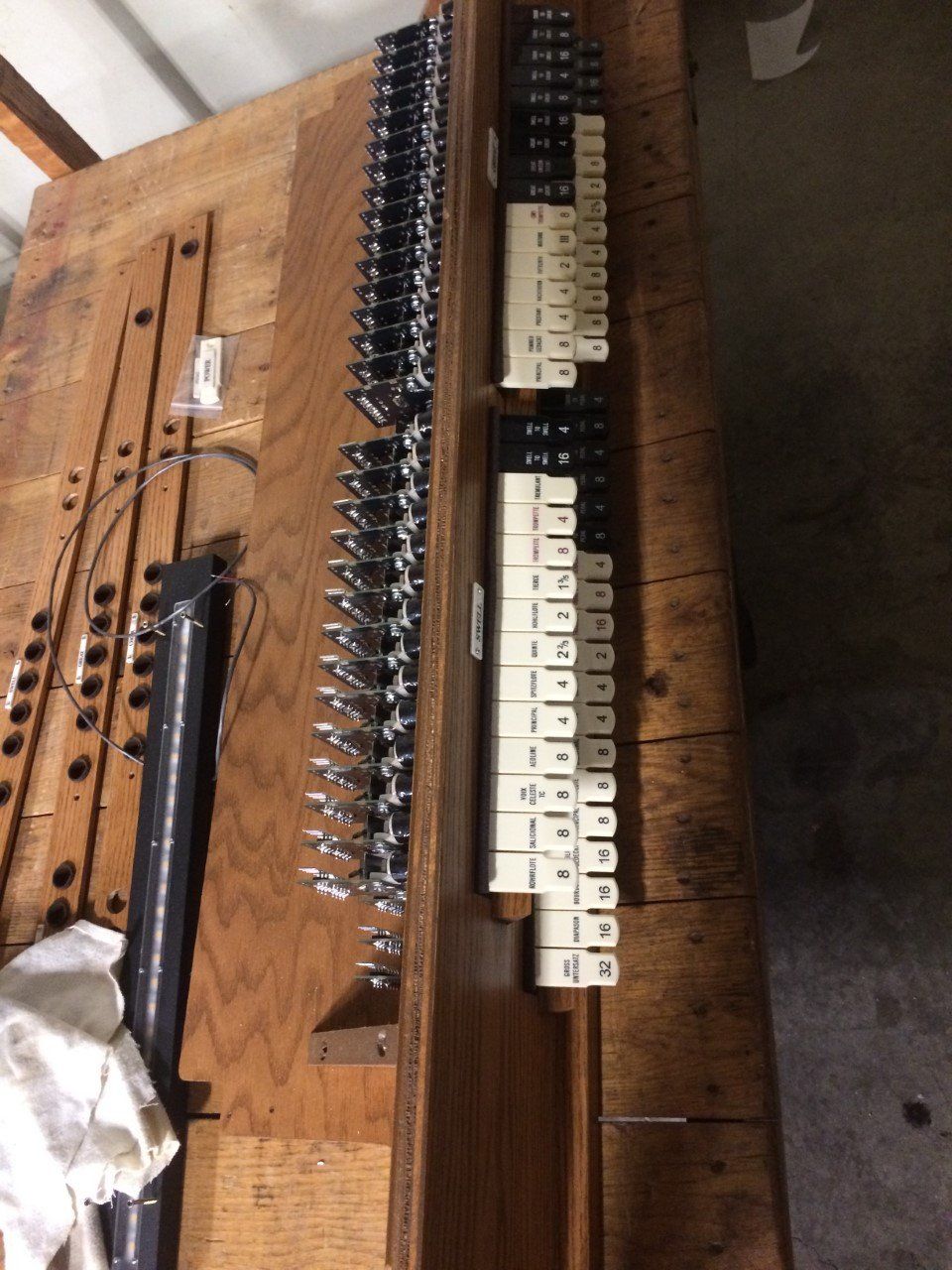 Wooden organ key mechanism with rows of white and black keys on a workbench.
