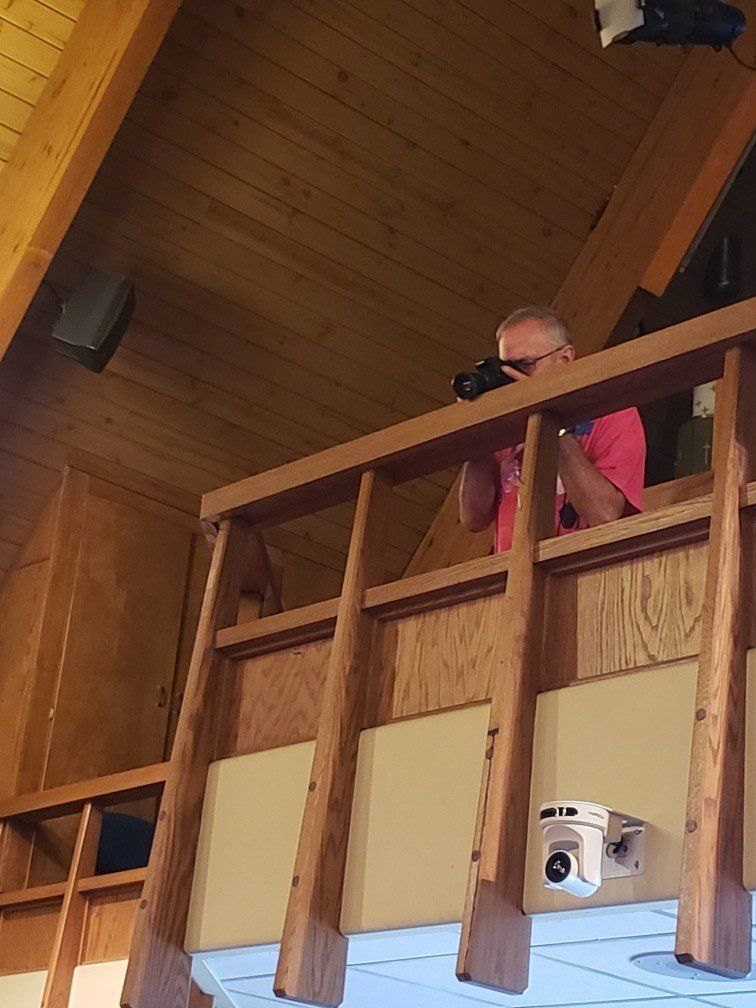Person in a pink top leaning on a wooden balcony inside a wooden room, taking a photo.