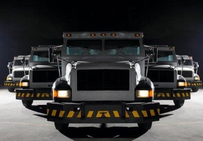 Armored trucks, lined up in formation, front view with yellow and black bumper guards.