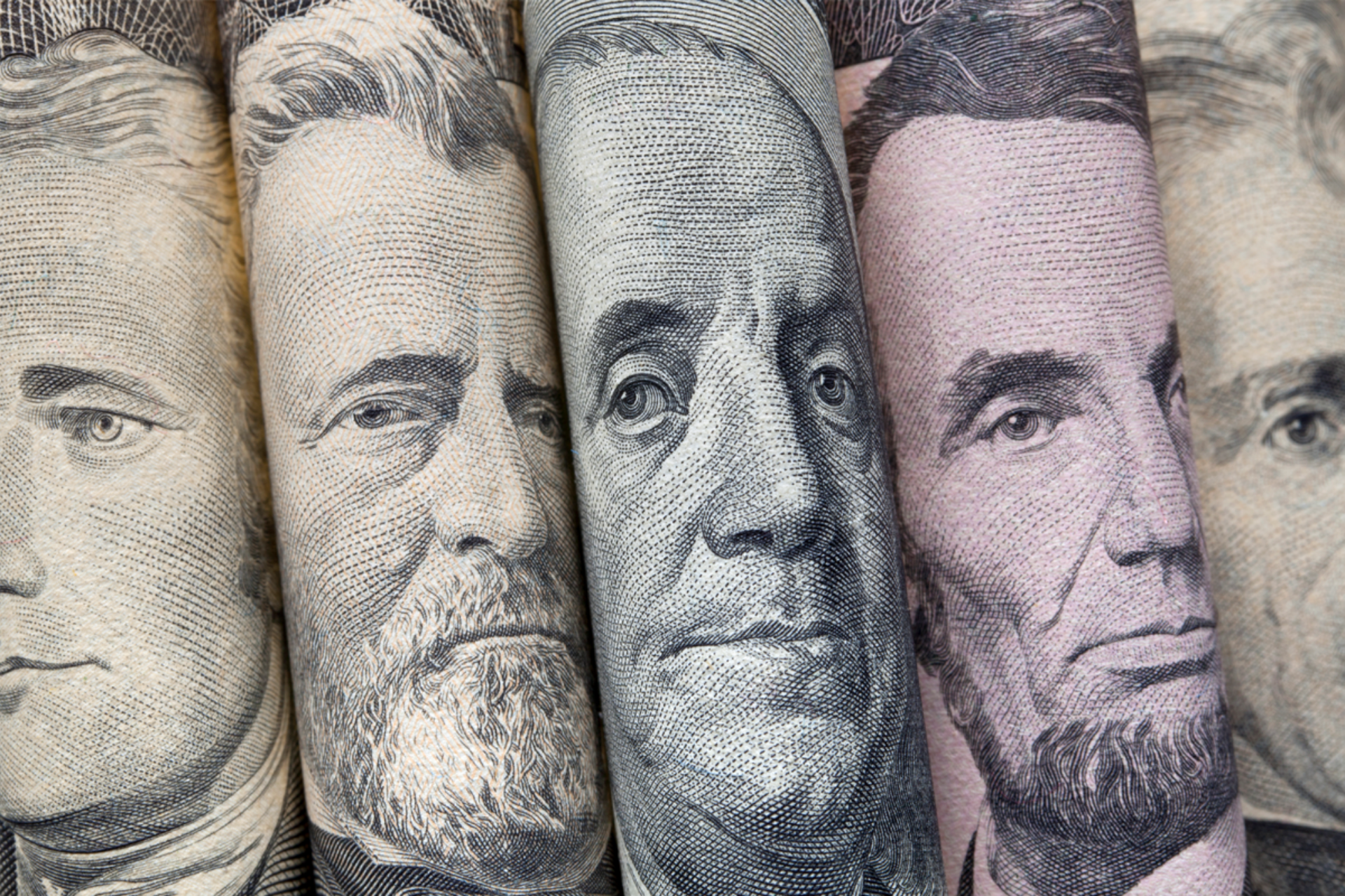 Rolled US bills showing portraits of historical figures.
