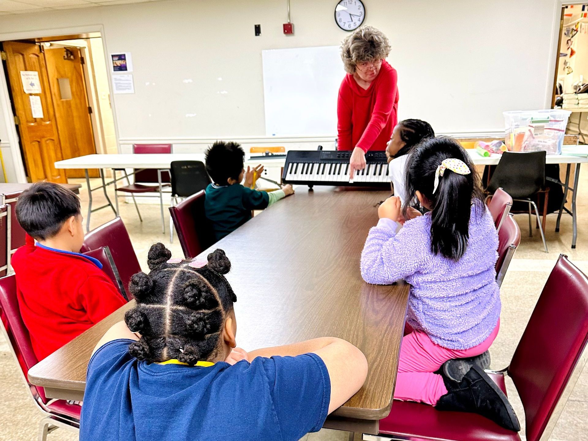 A woman is teaching a group of children how to play a keyboard.
