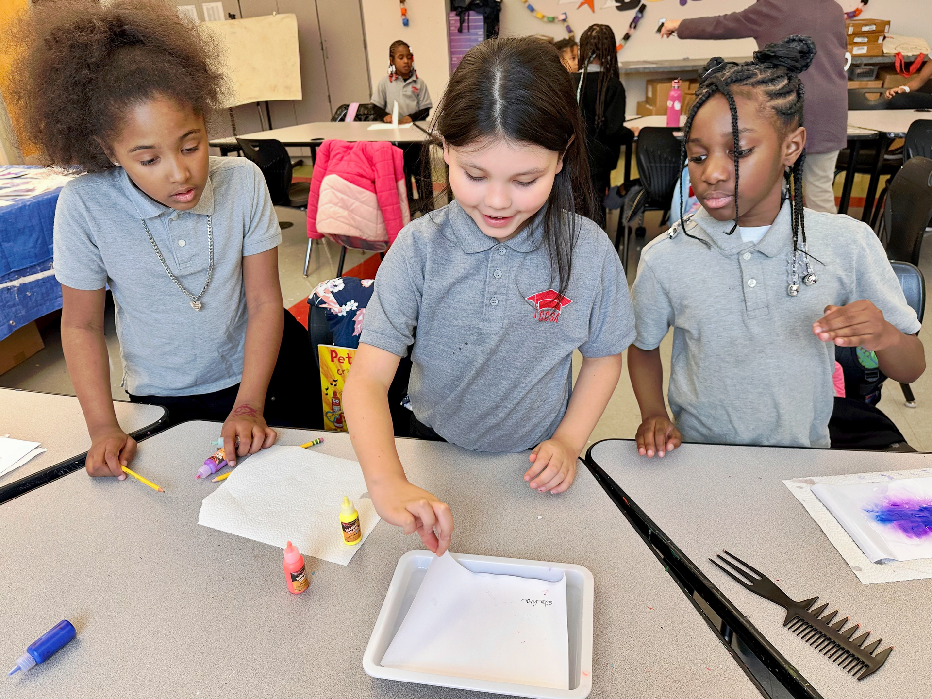 Three young girls are sitting at a table in a classroom.
