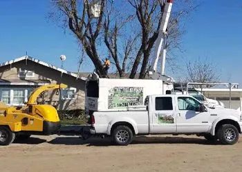 A white truck with a tree chipper attached to it is parked in front of a house.