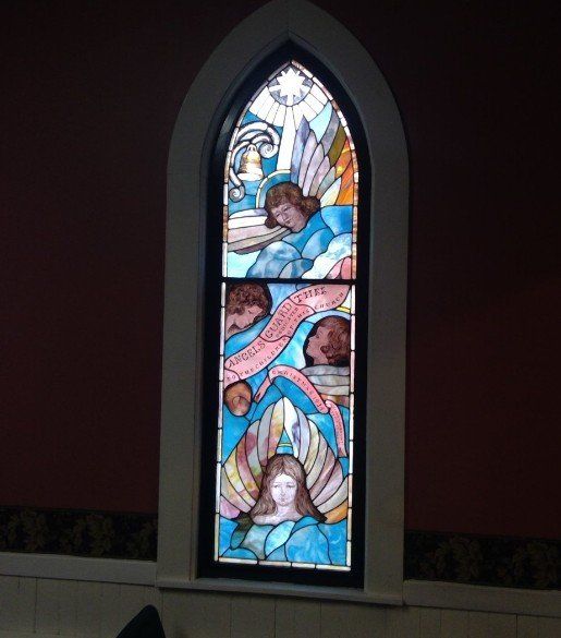Stained glass window depicting angels with blue wings against a blue background, inside a church.