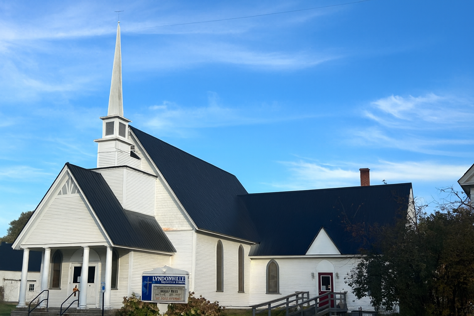 White church with steeple and dark roof against a blue sky.