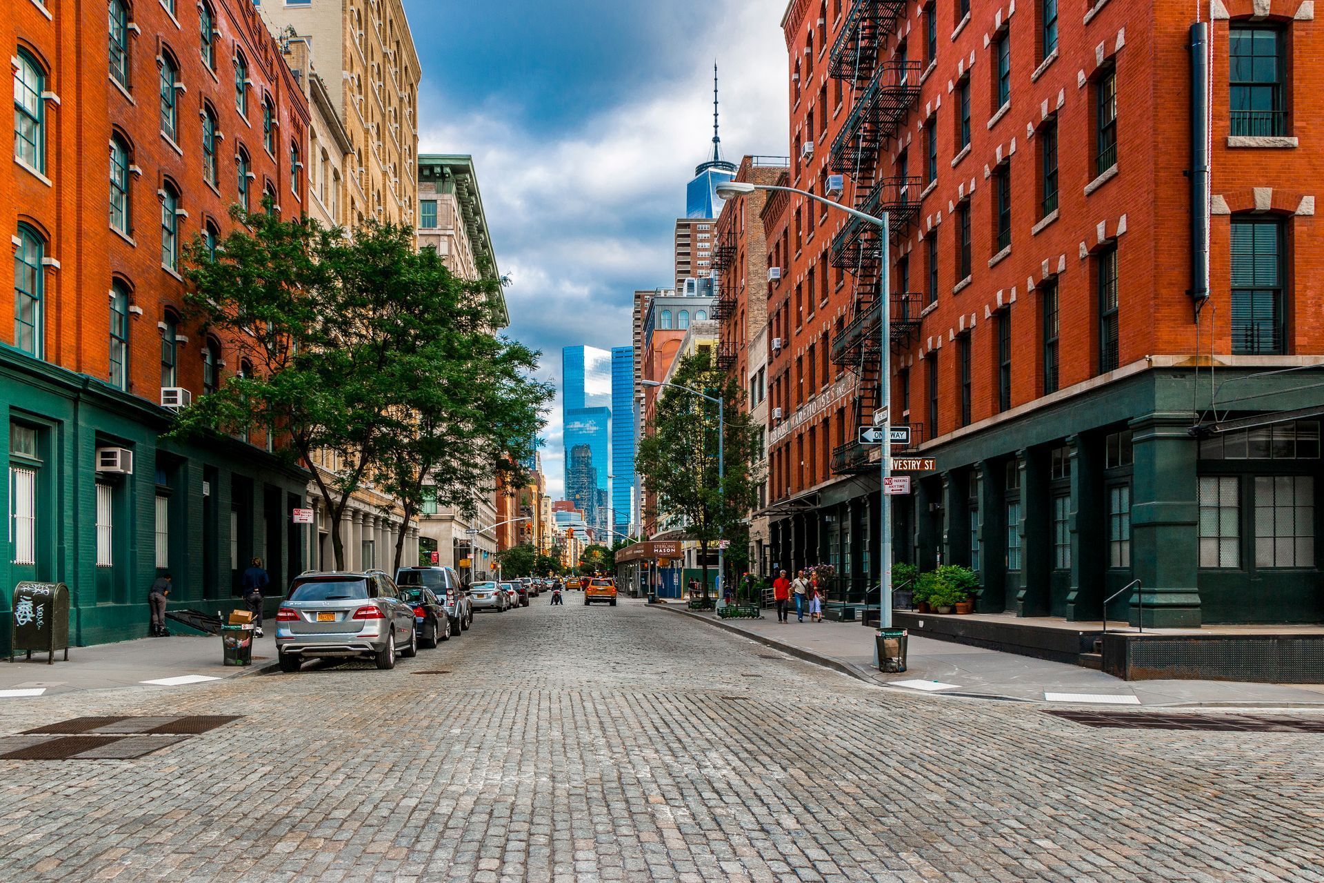 A cobblestone street in a city with cars parked on the side of it.