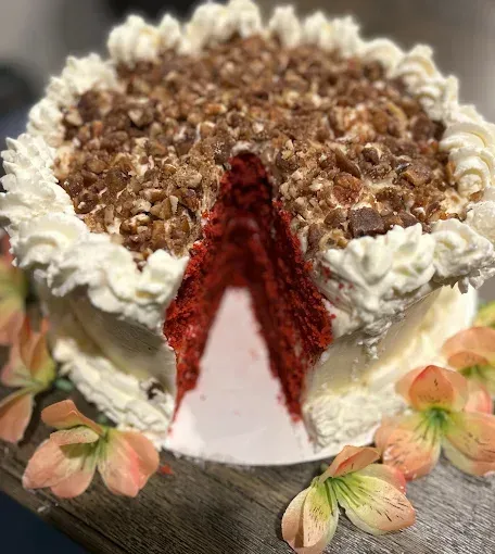 Red velvet cake with white frosting and chopped topping; slice cut out.