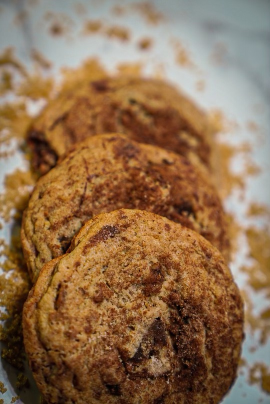 Three cinnamon sugar cookies in a row, with loose brown sugar around them.