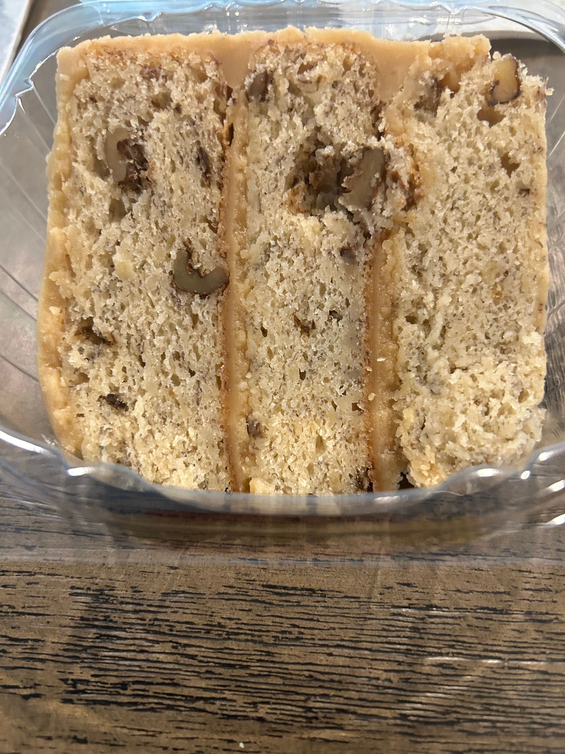 Slice of cake with walnuts and frosting, inside a clear plastic container.