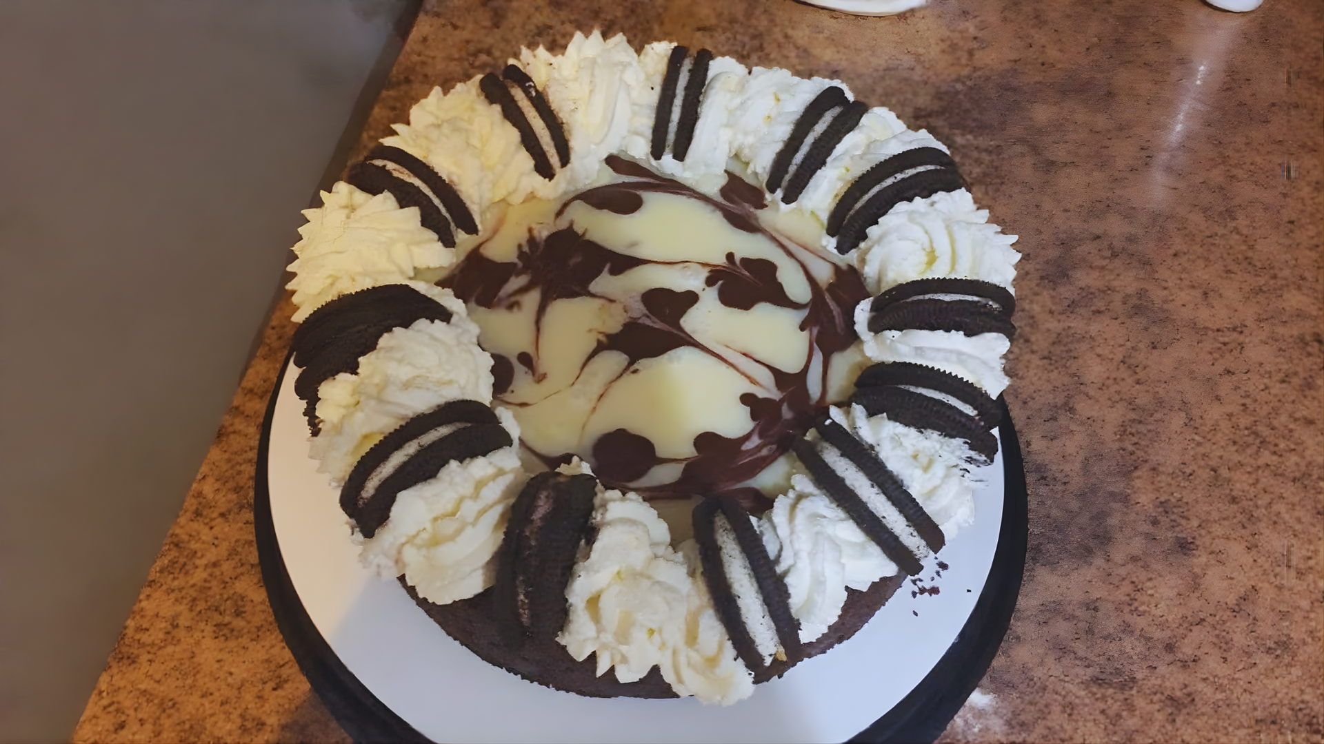 Chocolate cake with cream swirls and Oreo cookies on a counter.