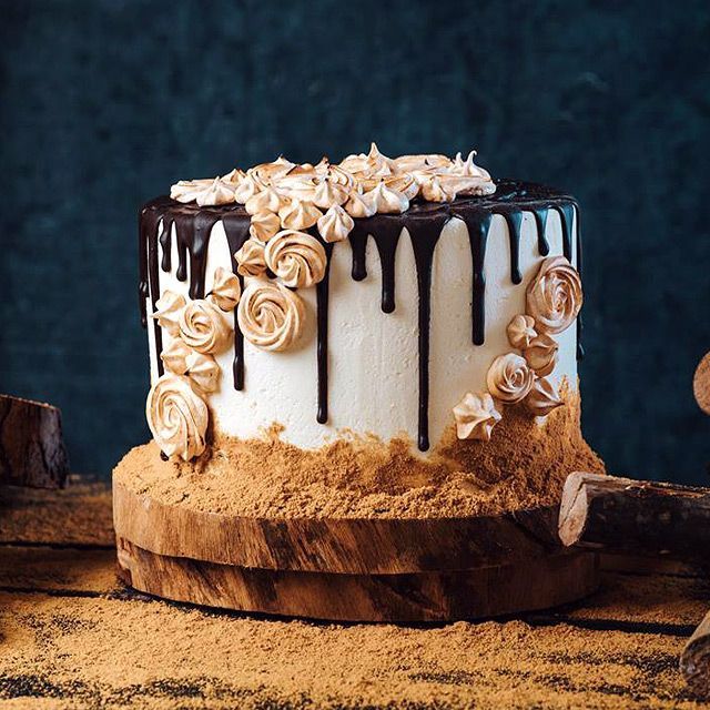 Cake with white frosting, chocolate drips, and caramel swirl decorations, on a wooden stand.