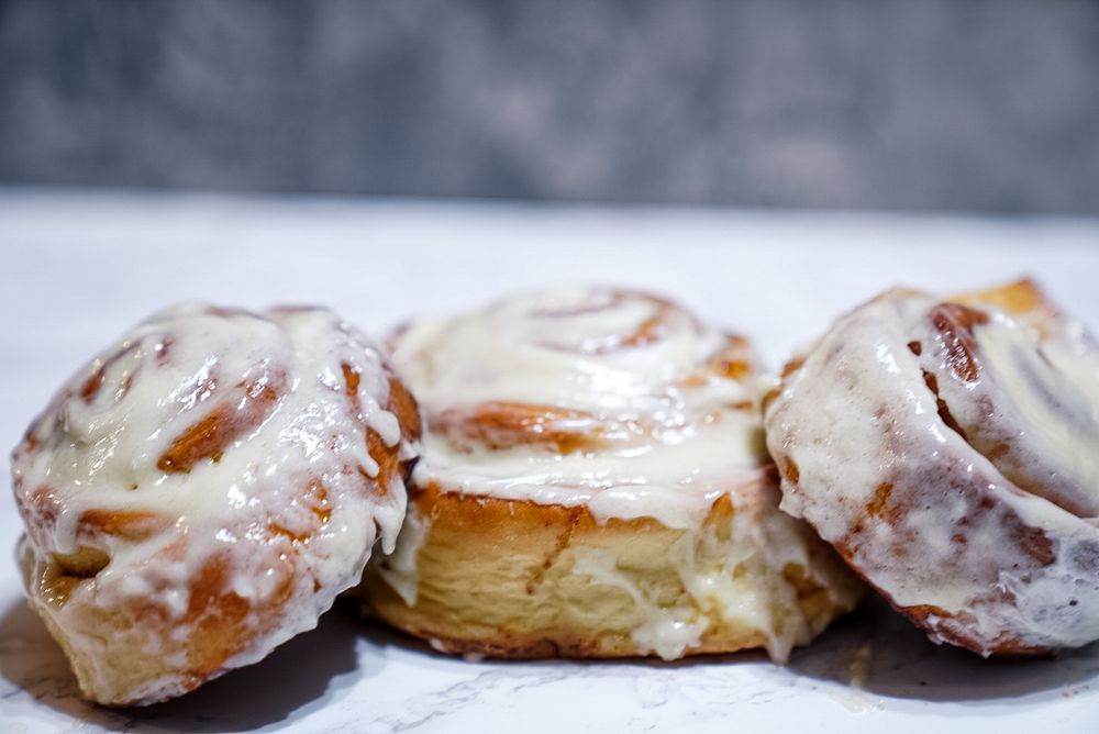 Three glazed cinnamon rolls on a white surface, with a blurred gray background.