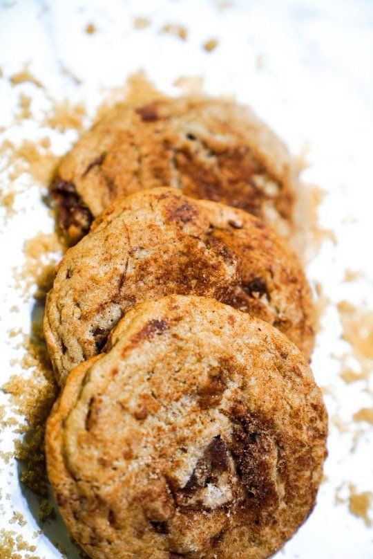 Three cinnamon-sugar cookies in a row, with scattered sugar on white surface.
