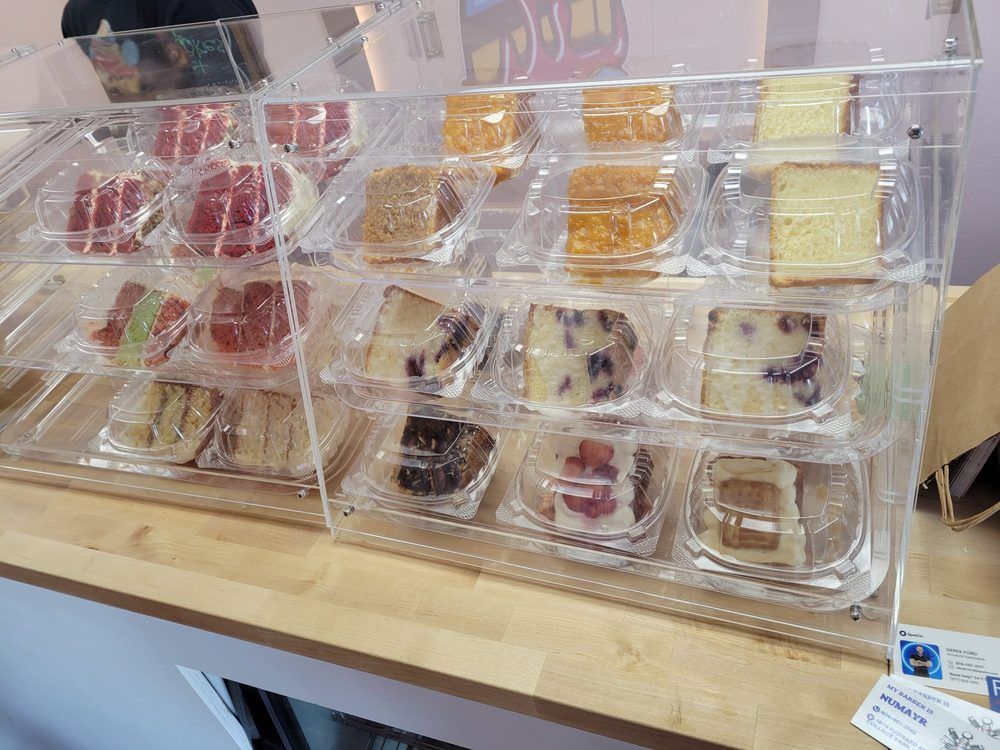 Display case with assorted cake slices in clear plastic containers.