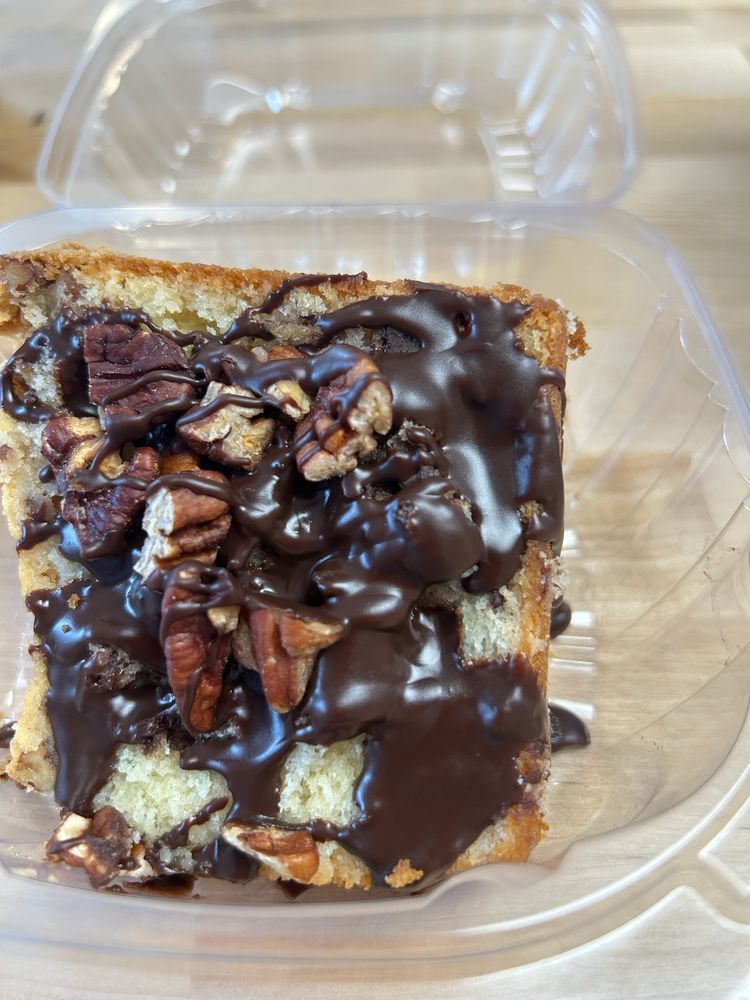 Slice of cake with chocolate frosting and pecans in a clear plastic container.