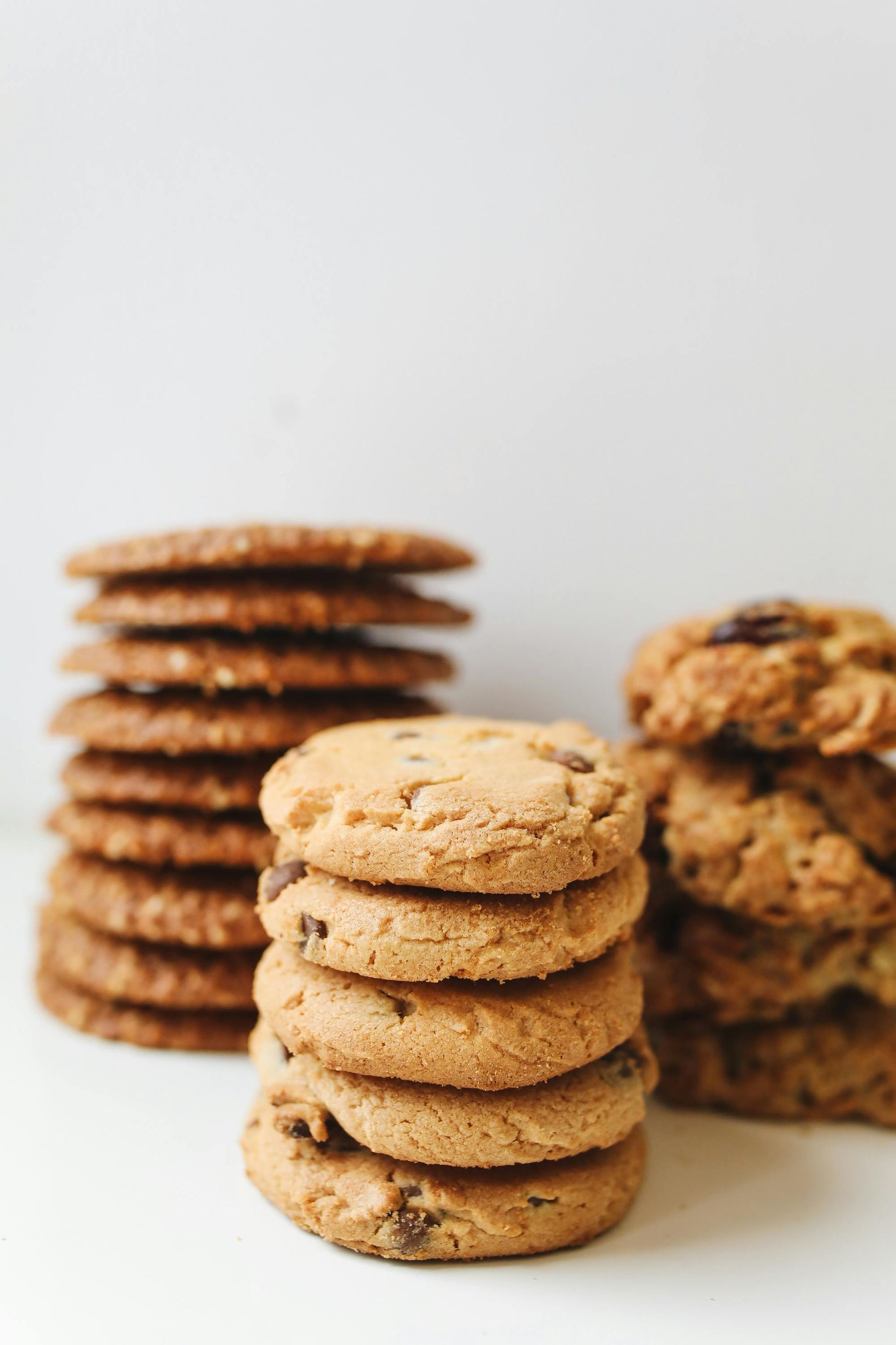 Three stacks of chocolate chip and oatmeal cookies on a white surface.