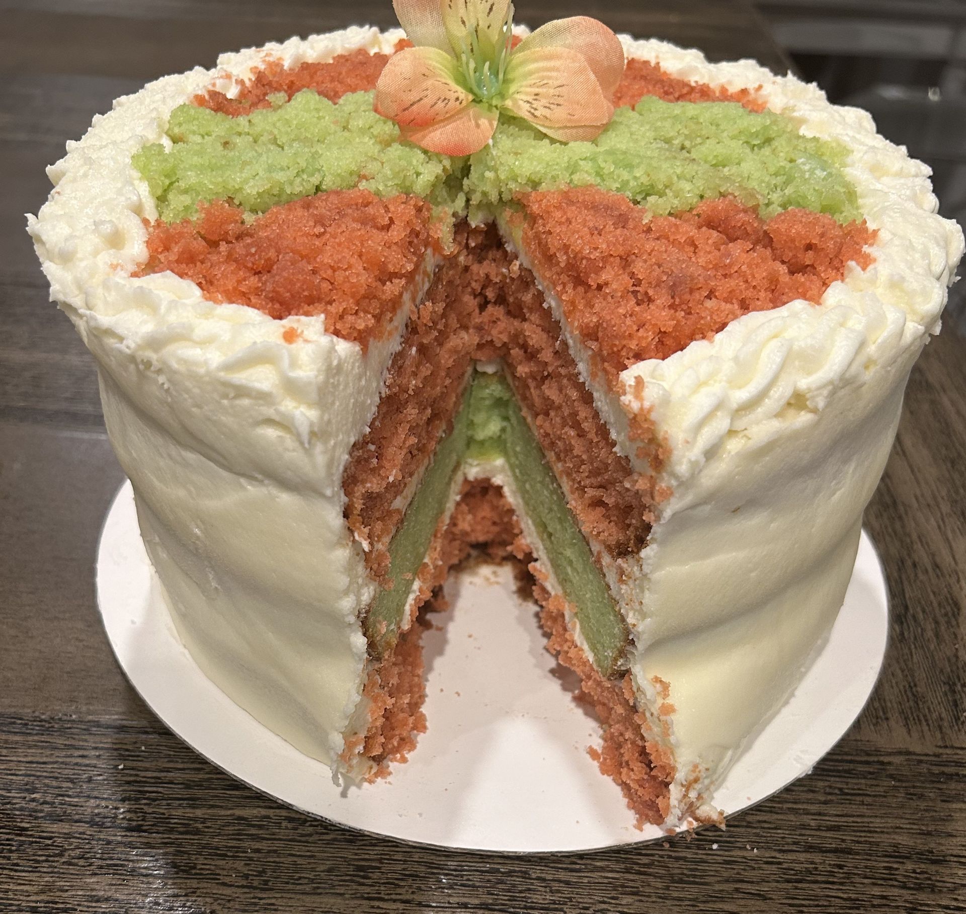 Cake with layers of pink and green, topped with sprinkles and flowers, partially sliced.