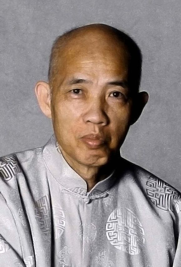 A bald man wearing a gray shirt is looking at the camera.
