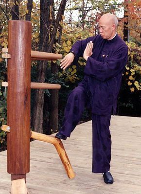 A man in a purple suit is standing next to a wooden dummy.