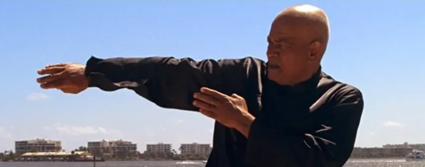 A bald man is standing on a balcony with his arms outstretched.