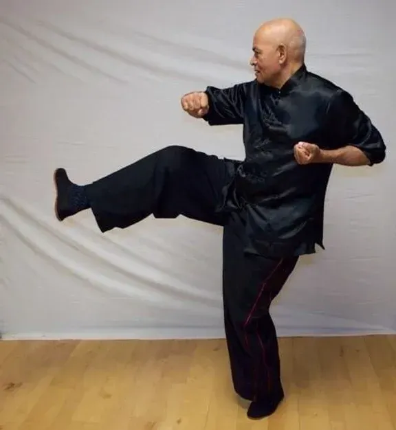 A bald man in a black shirt and black pants is kicking in the air