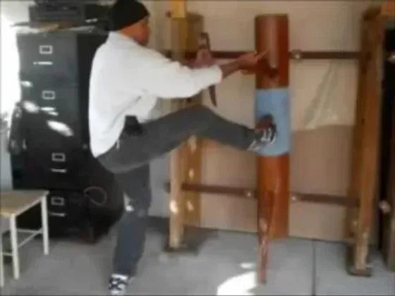 A man is kicking a wooden dummy in a room