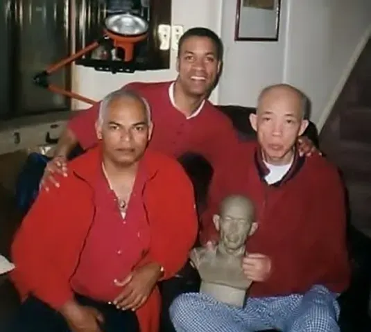 Three men are posing for a picture with a statue of a man