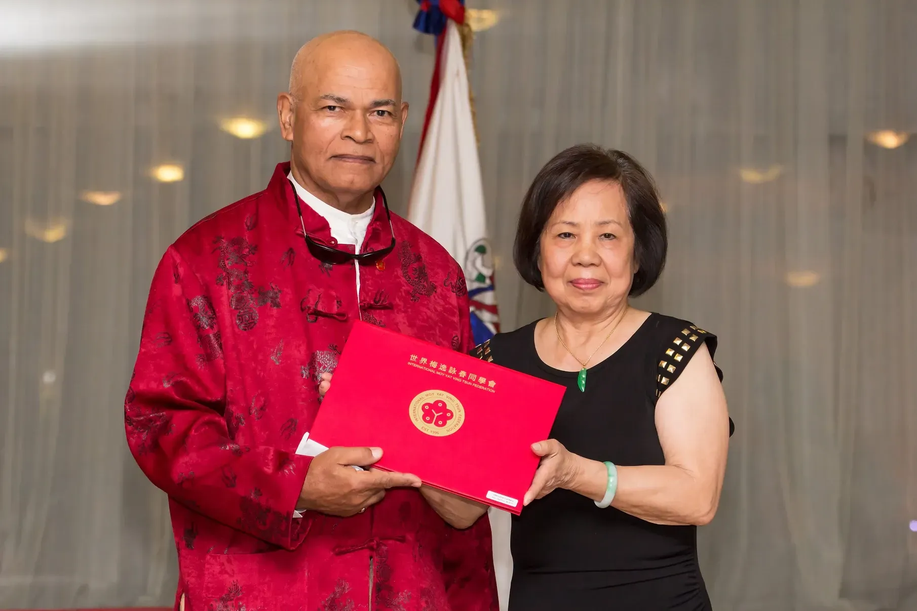 A man in a red jacket is giving a certificate to a woman in a black dress.