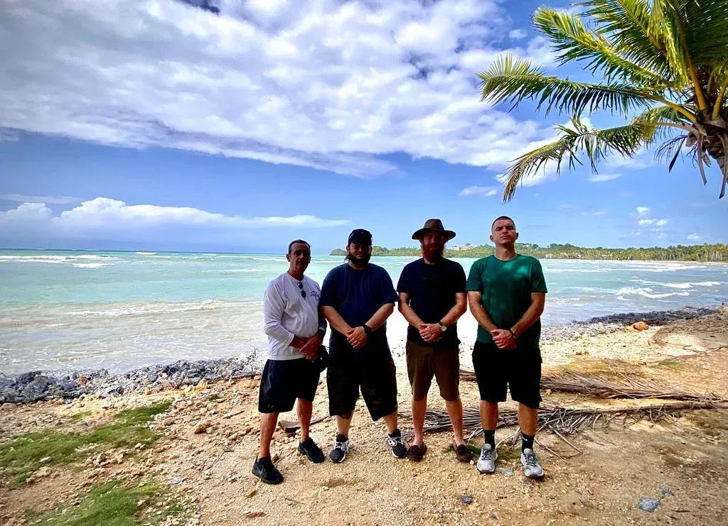Four men are posing for a picture on a beach.