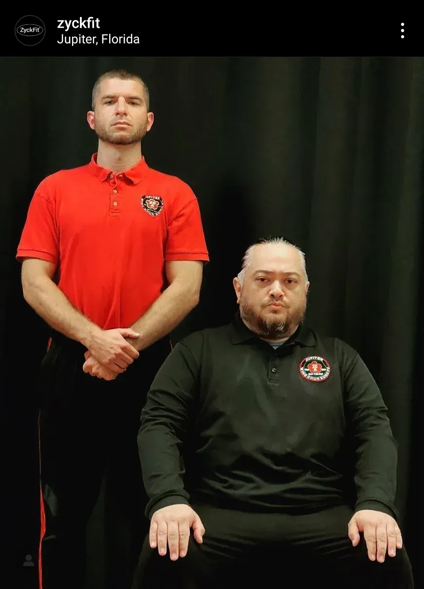 A man in a red shirt is standing next to another man in a black shirt.
