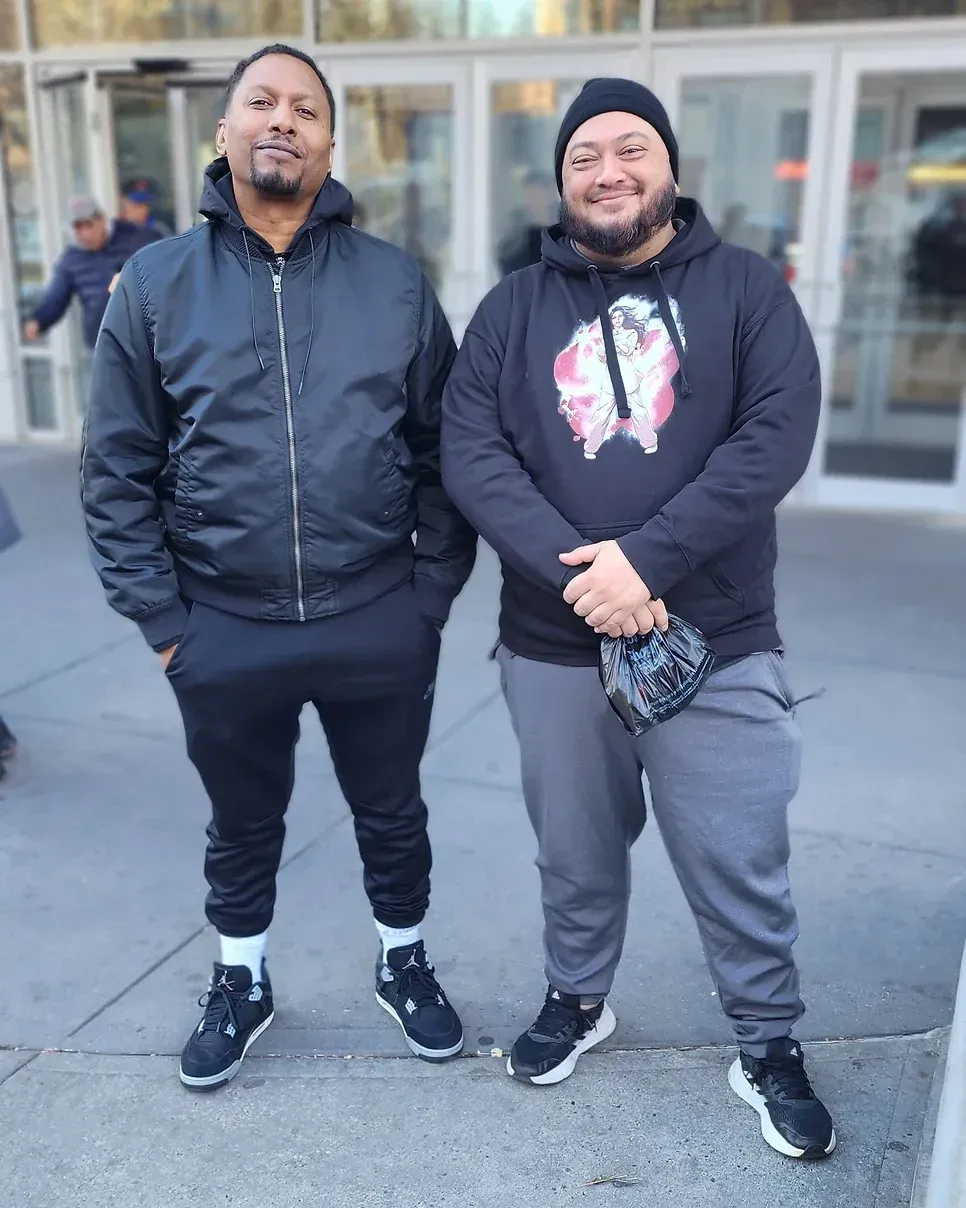 Two men are standing next to each other on a sidewalk in front of a building.
