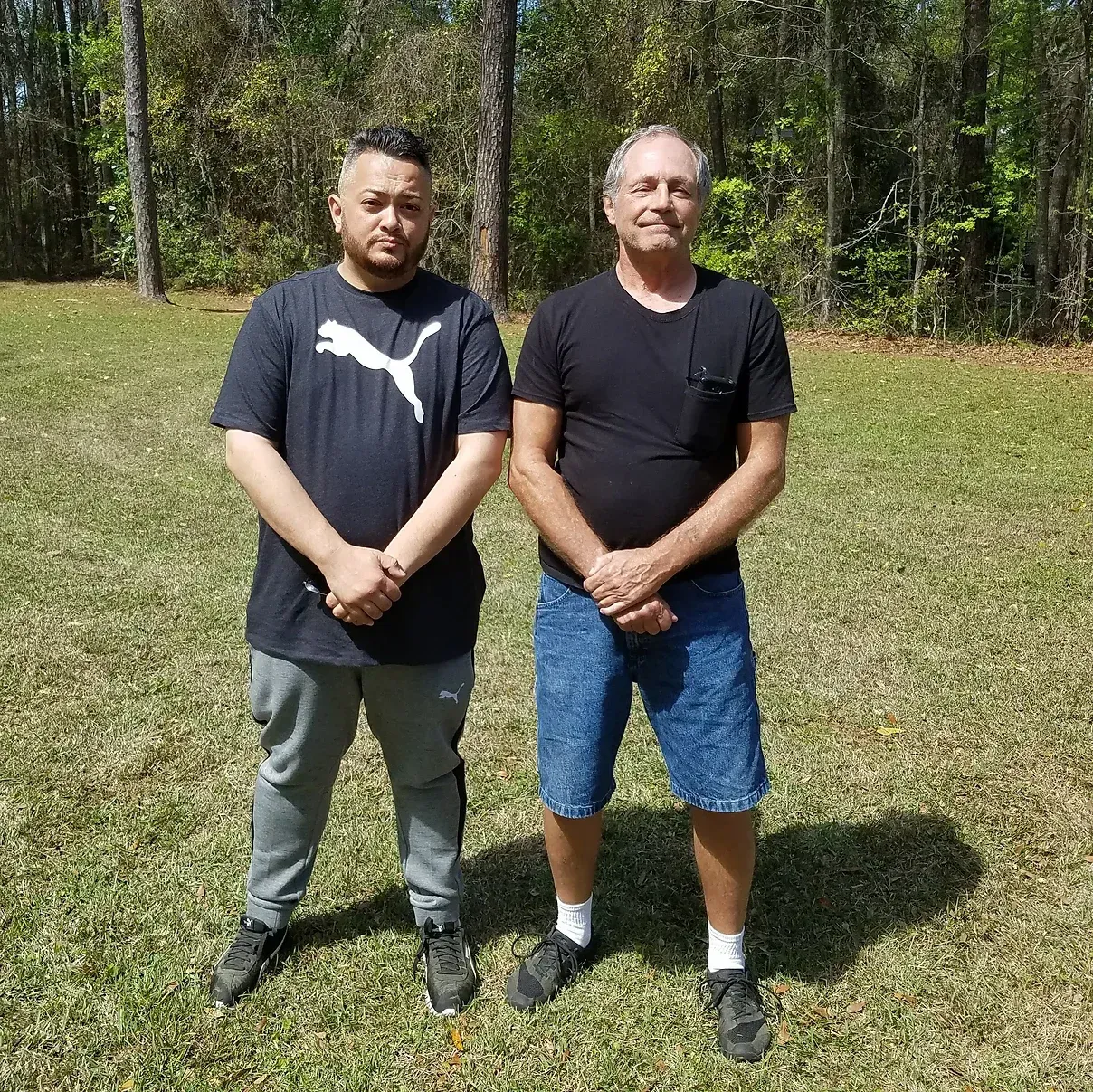 Two men are standing next to each other in a grassy field.