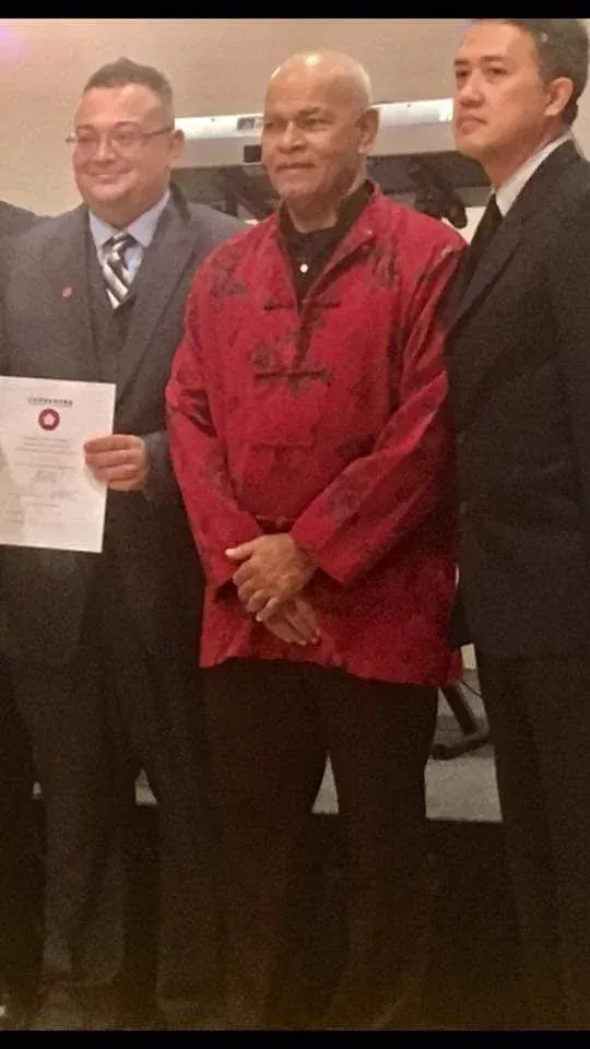 A man in a red jacket is standing next to two other men in suits.