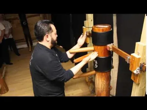 A man is standing next to a wooden dummy in a gym.