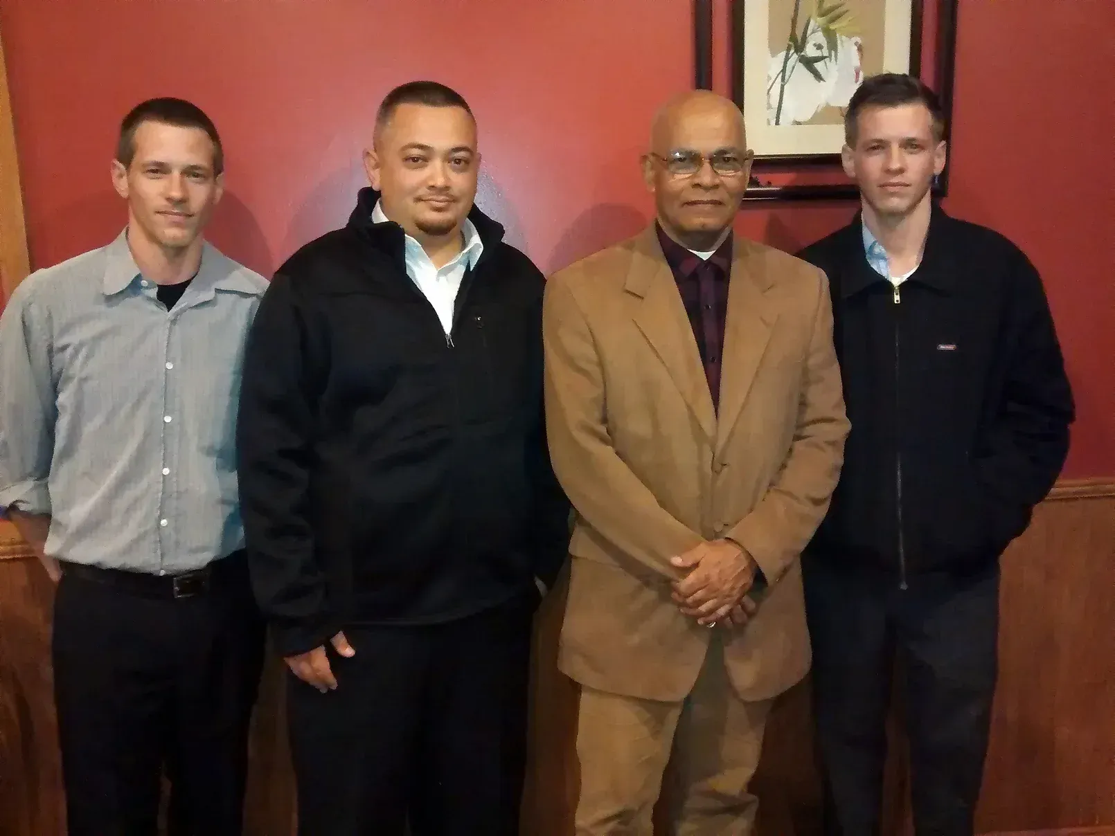 Four men are posing for a picture in front of a red wall