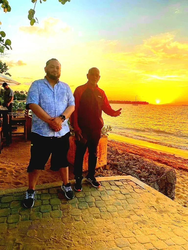 Two men are standing next to each other on a beach at sunset.