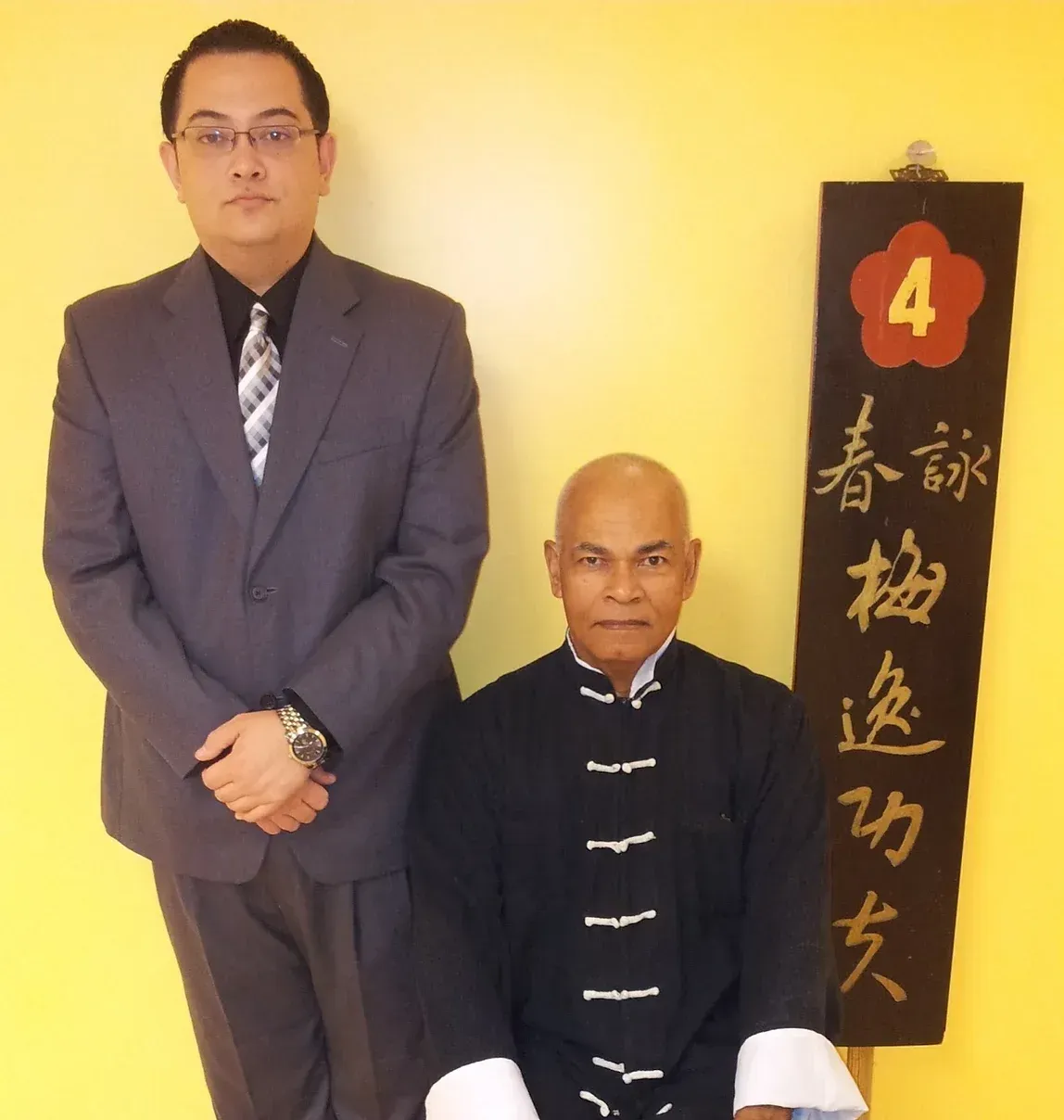 A man in a suit stands next to a man sitting in front of a sign that says 4