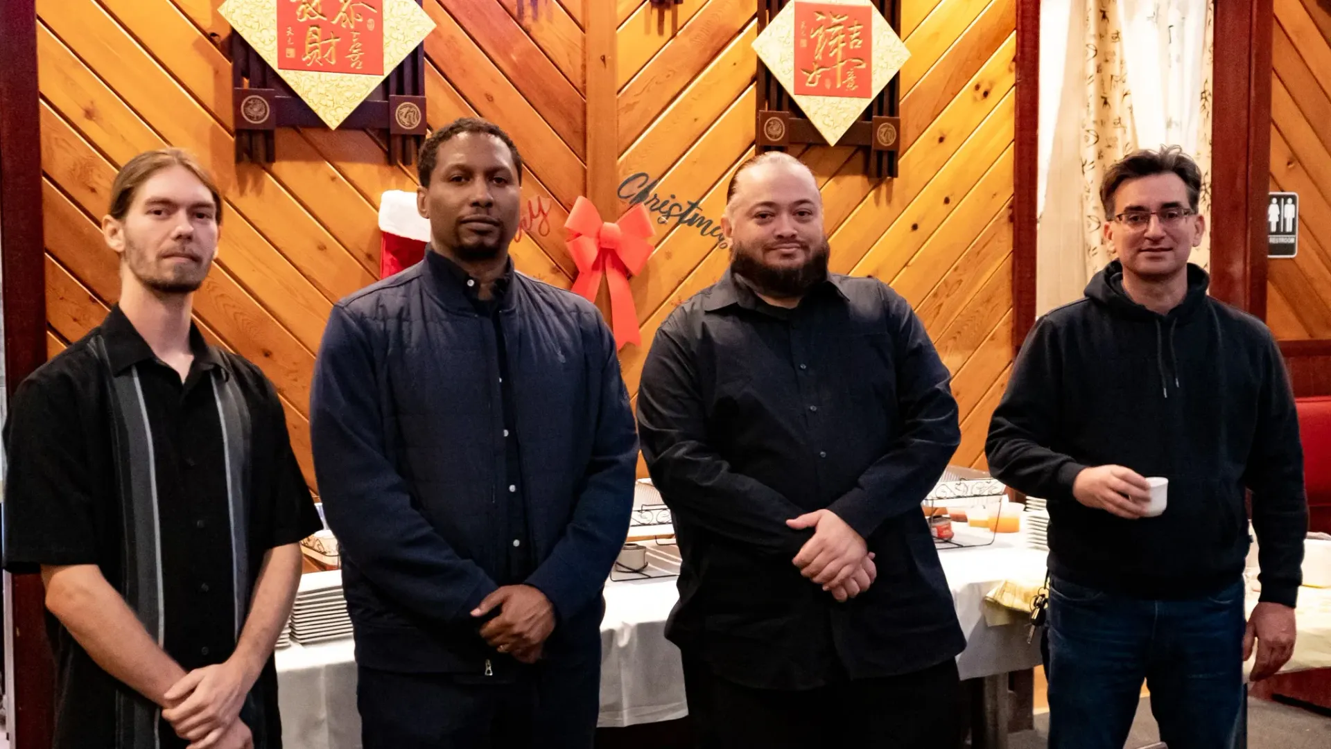 A group of men standing next to each other in front of a wooden wall.