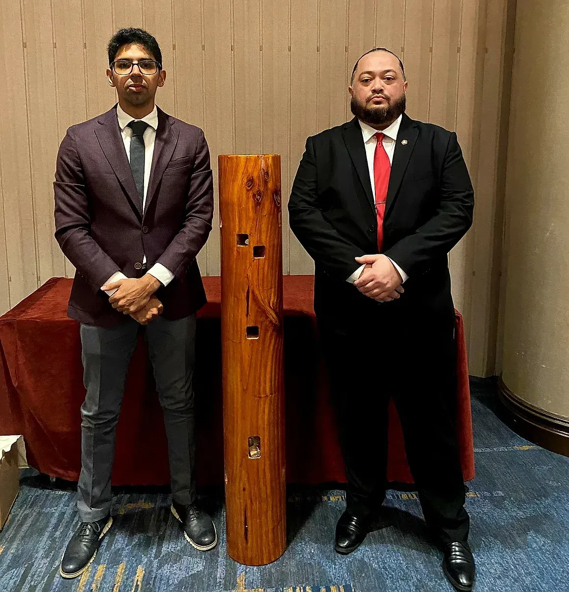 Two men in suits and ties are standing next to a wooden pole.